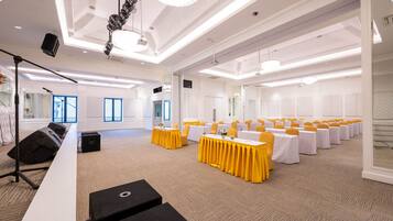 A conference room with rows of tables, yellow chairs, and a stage with a microphone.