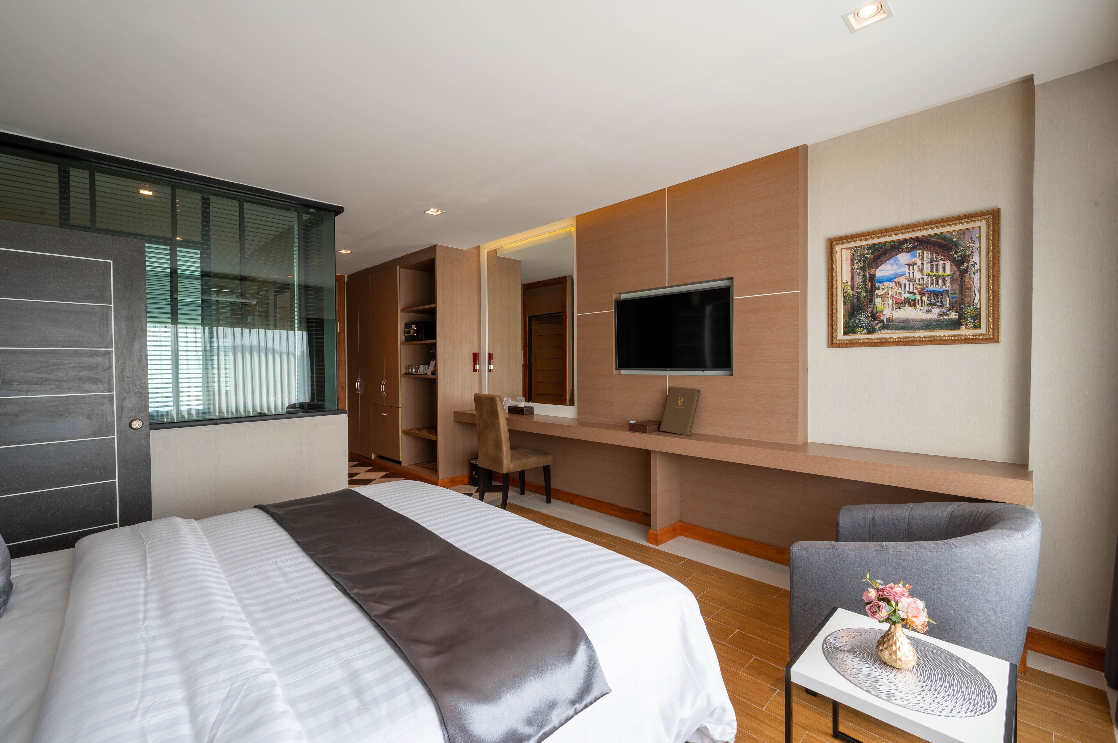 A hotel room with a large bed, a desk with a chair, a TV, and a painting on the wall.