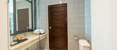 A modern bathroom with a glass shower enclosure, a wooden door, and a white toilet.