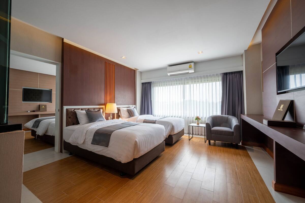 A modern hotel room with two beds, a desk, a chair, a TV, and an air conditioning unit.