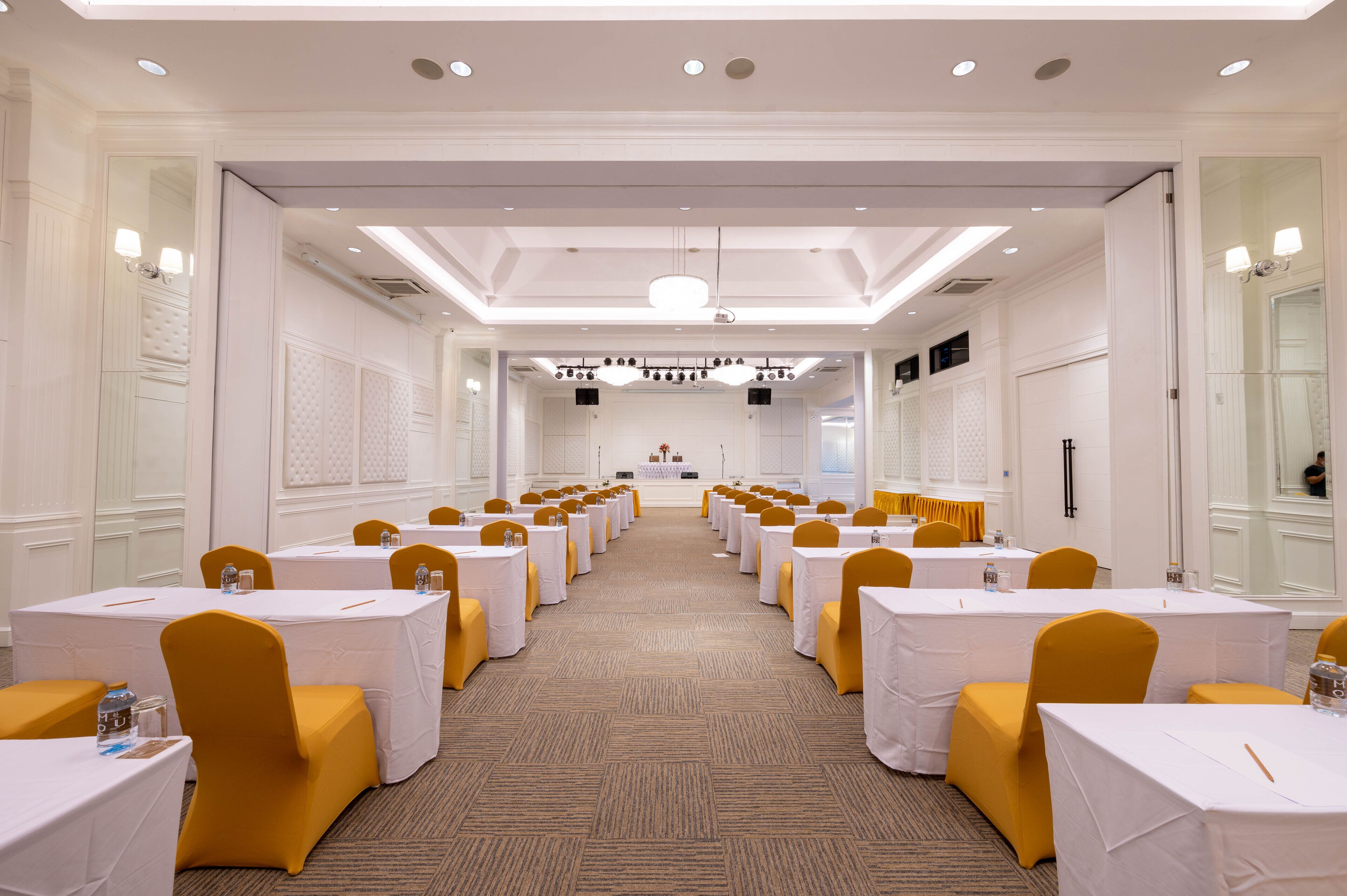 A conference room with rows of tables and chairs, a podium at the front, and a carpeted floor.