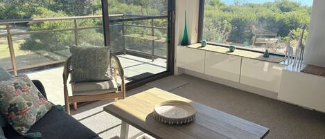 A balcony with a view of the sea and greenery, furnished with a sofa, chair, and table.