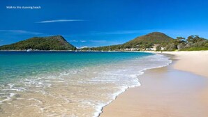 Uma praia com águas turquesa cristalinas, areal arenoso e paisagem montanhosa ao fundo.