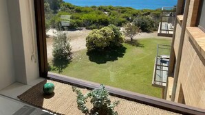 Vista de uma varanda com vista para um jardim bem cuidado, céu azul límpido e uma ilha ao longe.