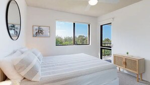 Quarto com uma cama grande, um ventilador de teto, uma janela e vista para o verde lá fora.