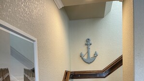 Una escalera con escalones de madera y barandilla blanca, una decoración de ancla montada en la pared y un cuadro enmarcado de una escalera.