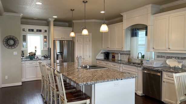Una cocina amplia con una isla central, muebles blancos y un refrigerador de acero inoxidable.