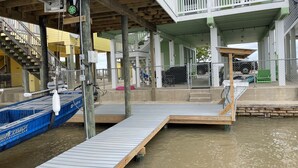 Un muelle con un barco, un pasillo cubierto y un edificio con techo verde y barandillas blancas.