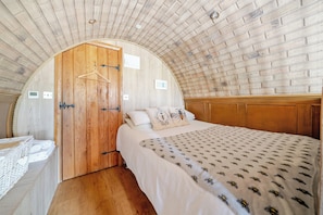 A bedroom with a wooden door, a bed with a patterned bedspread, and a wooden ceiling. - Luxury Pod-Sleeps 2-Hot Tub-Pets-Garden (Sheerness)