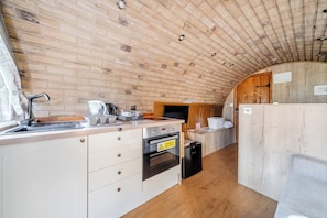 A compact kitchen with a brick wall, wooden ceiling, and a small dining area. - Luxury Pod-Sleeps 2-Hot Tub-Pets-Garden (Sheerness)
