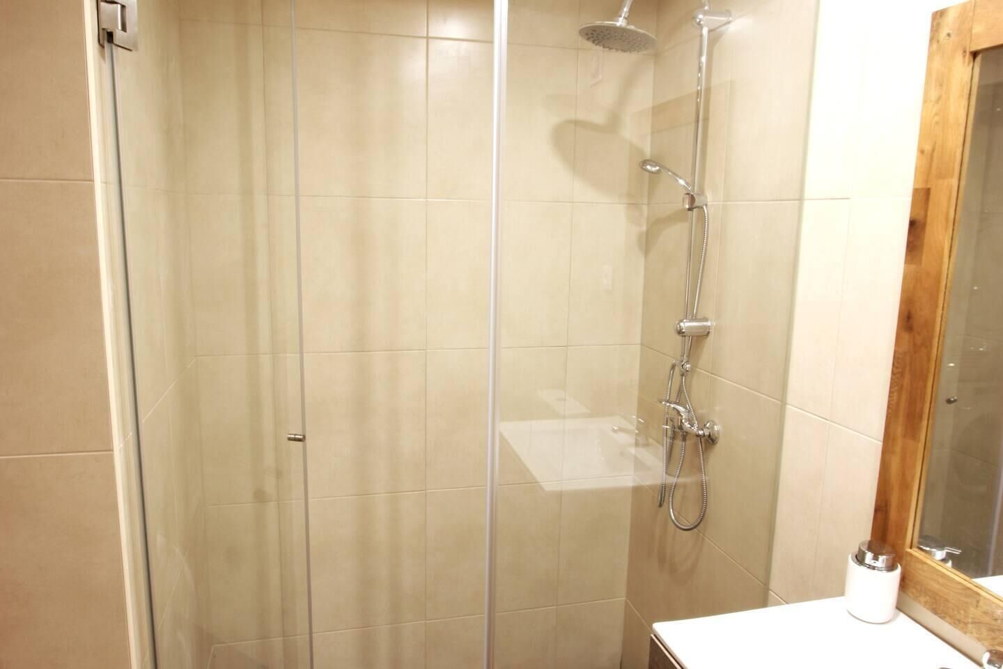 A glass-enclosed shower with a handheld showerhead and a wall-mounted faucet.