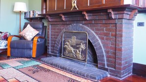 A living room with a brick fireplace, a leather armchair, a patterned rug, and a bookshelf. - BALMORAL LODGE  - EXCLUSIVE COUNTRY ESCAPE (Cockatoo Valley)