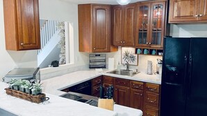 A kitchen with wooden cabinets, a black refrigerator, a sink, and a countertop with a plant and knives. - Light & airy home w/private hot tub on golf course (Quinton)