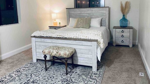 A bedroom with a bed, a nightstand, a lamp, a vase, and a patterned rug.