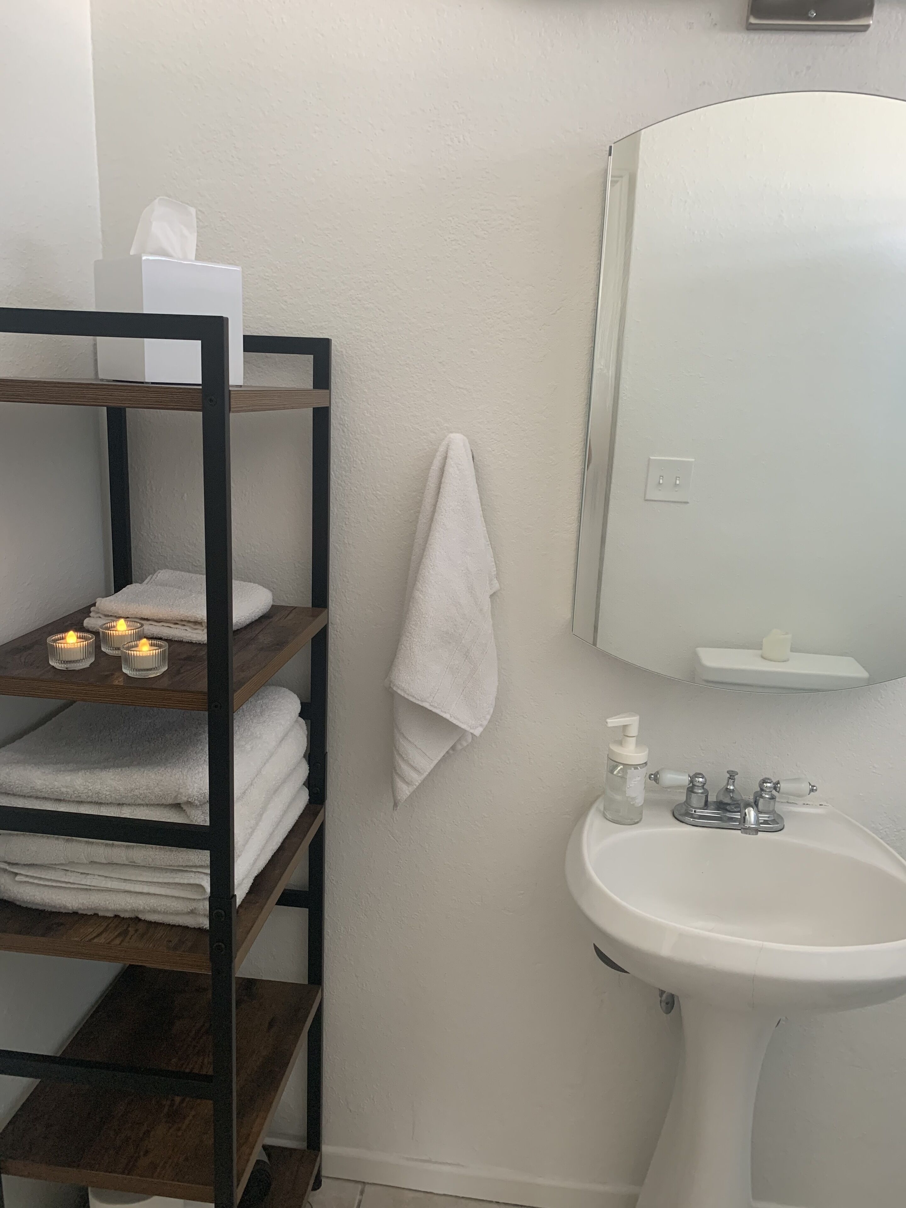 Une salle de bain équipée d’un lavabo, d’un miroir, d’un porte-serviettes et d’étagères où sont pliées des serviettes.