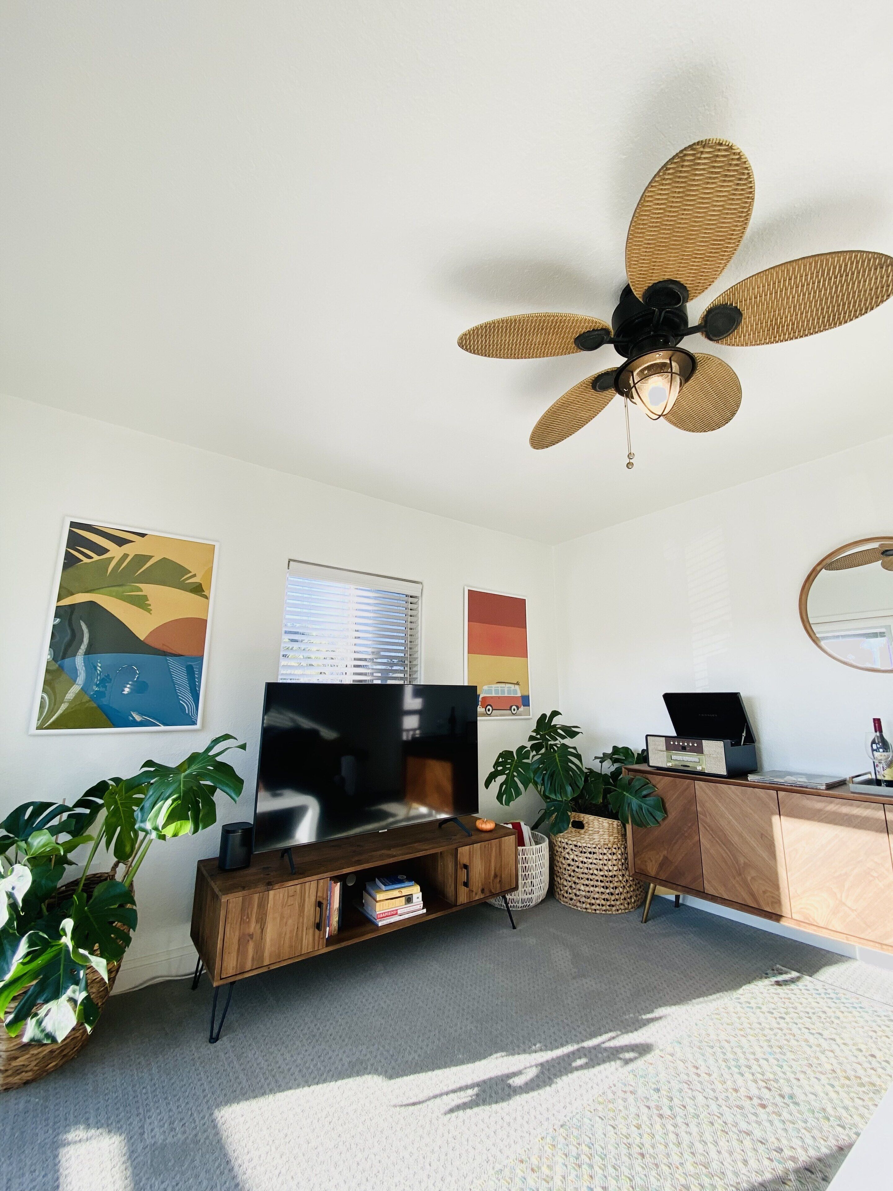 Ein Wohnzimmer mit Flachbildfernseher, Holzschrank, Topfpflanzen und Deckenventilator.