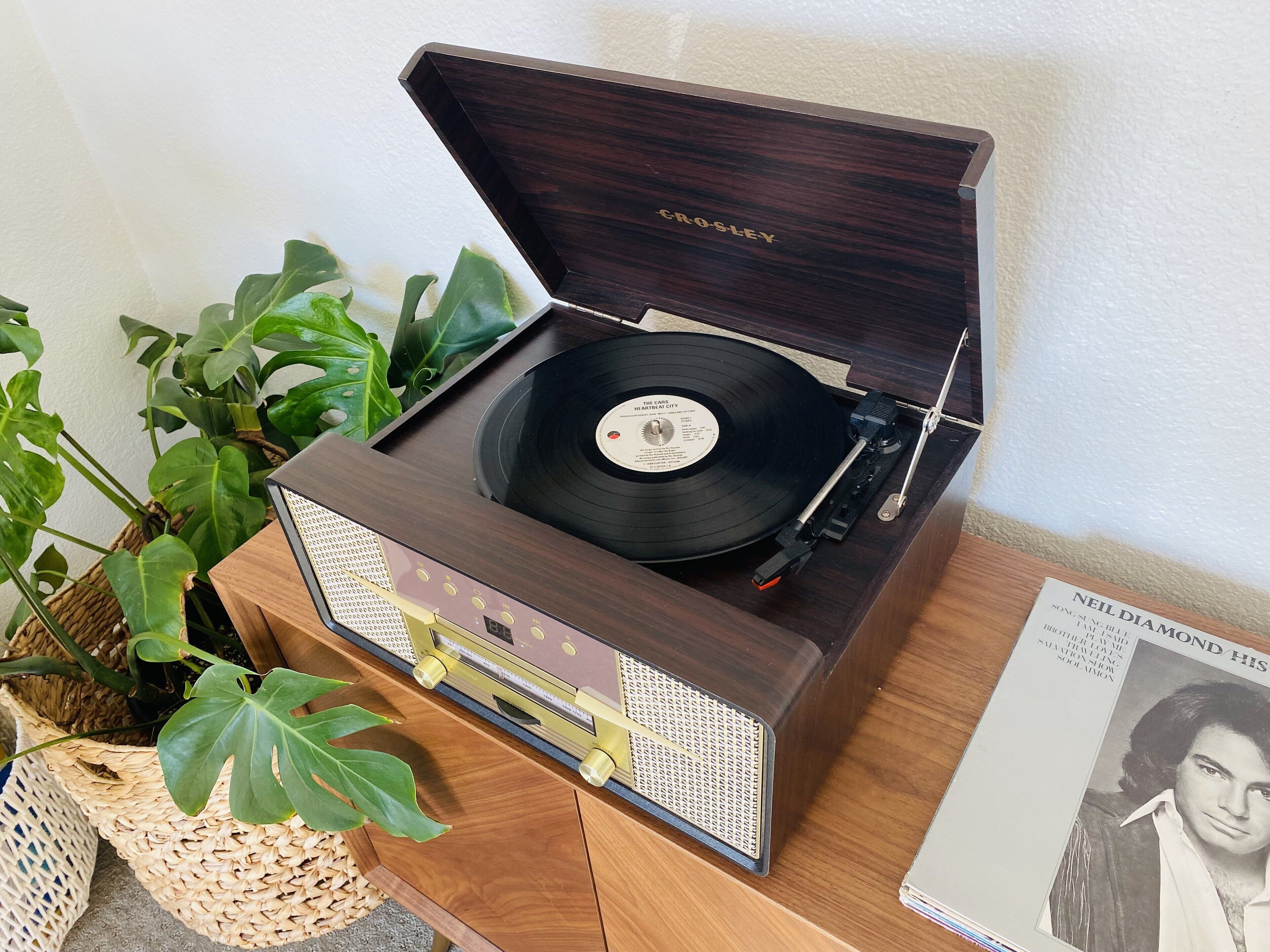 A vintage Crosley turntable with a vinyl record, placed on a wooden cabinet.