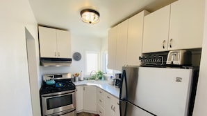 A compact kitchen with white cabinets, a stainless steel stove, a refrigerator, and a toaster.