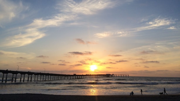 A pier extending into the ocean with the sun setting in the background.