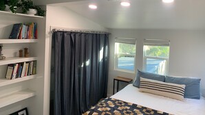 A bedroom with a bed, a bookshelf, a window, and a ceiling light.