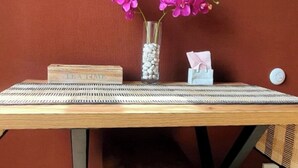 Un tavolo di legno con un sottotavolo intrecciato, un vaso con fiori viola e un portascopini.