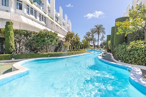 A swimming pool with a curved edge, surrounded by well-maintained hedges and palm trees.