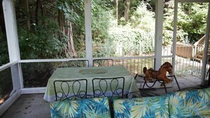 Eine überdachte Terrasse mit Tisch und Stühlen, umgeben von Grünpflanzen.