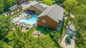 An aerial view of a resort with a swimming pool, outdoor seating, and a large building with multiple floors. - ONE Minute from Silver Dollar City! INDOOR Pool! (Branson)