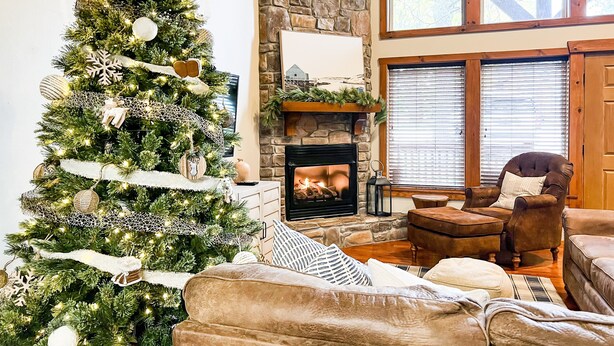 A cozy living room with a large Christmas tree, a stone fireplace, leather sofas, and a high ceiling with wooden beams. - ONE Minute from Silver Dollar City! INDOOR Pool! (Branson)