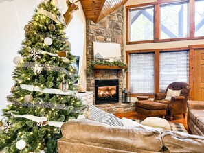 A cozy living room with a large Christmas tree, a stone fireplace, leather sofas, and a high ceiling with wooden beams. - ONE Minute from Silver Dollar City! INDOOR Pool! (Branson)