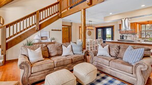 A spacious living area with a large brown sofa set, a wooden staircase, and a kitchen in the background. - ONE Minute from Silver Dollar City! INDOOR Pool! (Branson)
