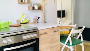 A modern kitchen with wooden cabinets, a built-in oven, and a dining area with a white chair. - Cozy Studio close to seaside and city center (Palaio Faliro)