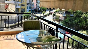 A balcony with a glass table and chairs, overlooking a street with buildings and a parked car. - Cozy Studio close to seaside and city center (Palaio Faliro)