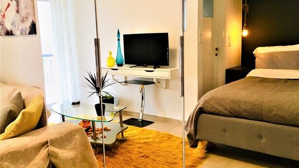 A modern hotel room with a glass partition separating the living area from the bedroom. - Cozy Studio close to seaside and city center (Palaio Faliro)