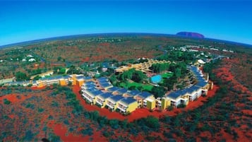 An aerial view of a resort with multiple buildings arranged in a semi-circular layout, surrounded by red vegetation and a clear blue sky.