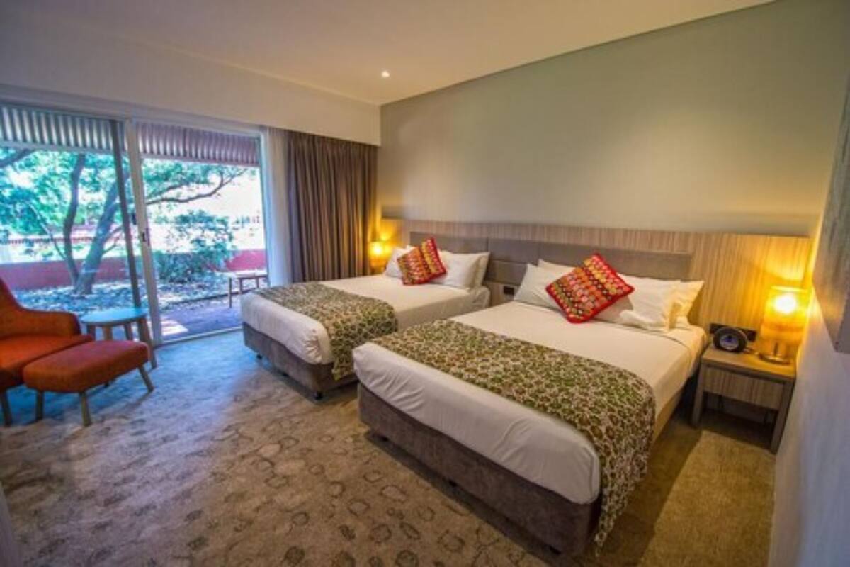 A hotel room with two beds, a sofa, a small table, and a view of the outdoors.