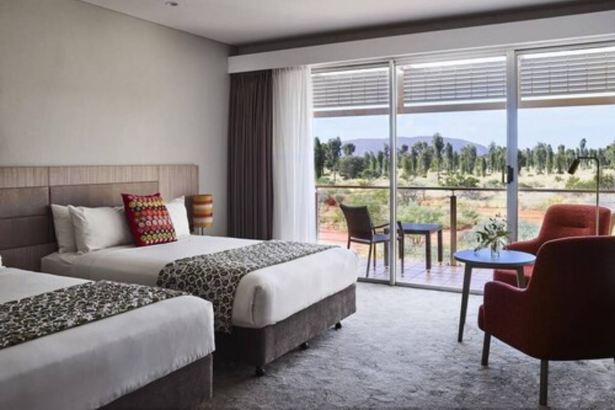 A hotel room with two beds, a sofa, a dining table, and a view of the outdoors.