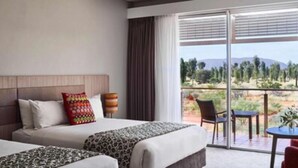 Habitación de hotel con cama, sofá, balcón con mesa y sillas, y vista a un paisaje.