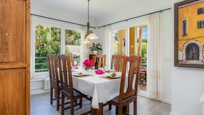 Un coin repas avec une table dressée pour quatre personnes, des chaises en bois, un luminaire suspendu et une vue sur la verdure à l’extérieur.