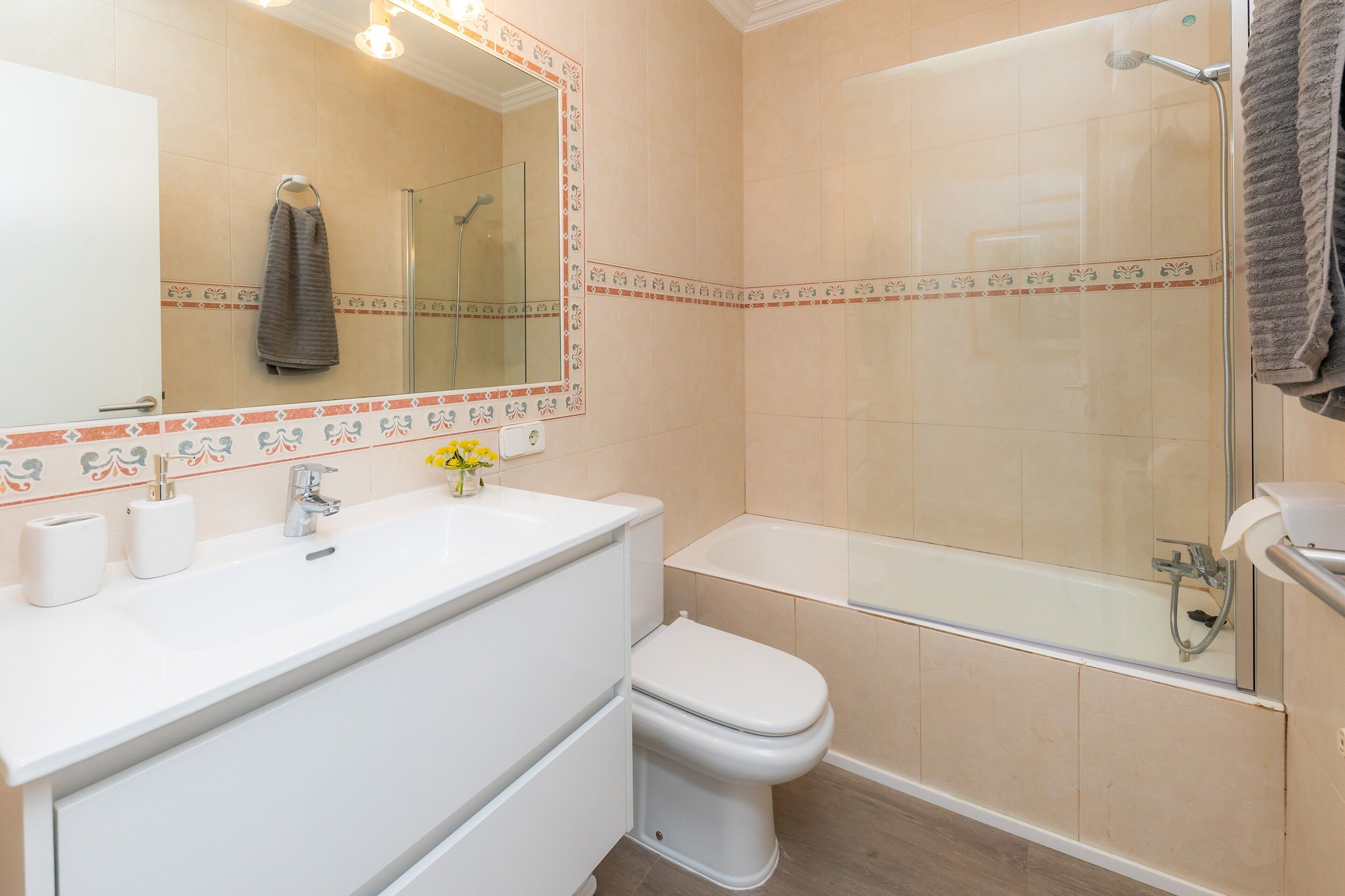 Un baño con lavamanos, inodoro y bañera blancos, ducha con puerta de vidrio y espejo con marco decorativo.