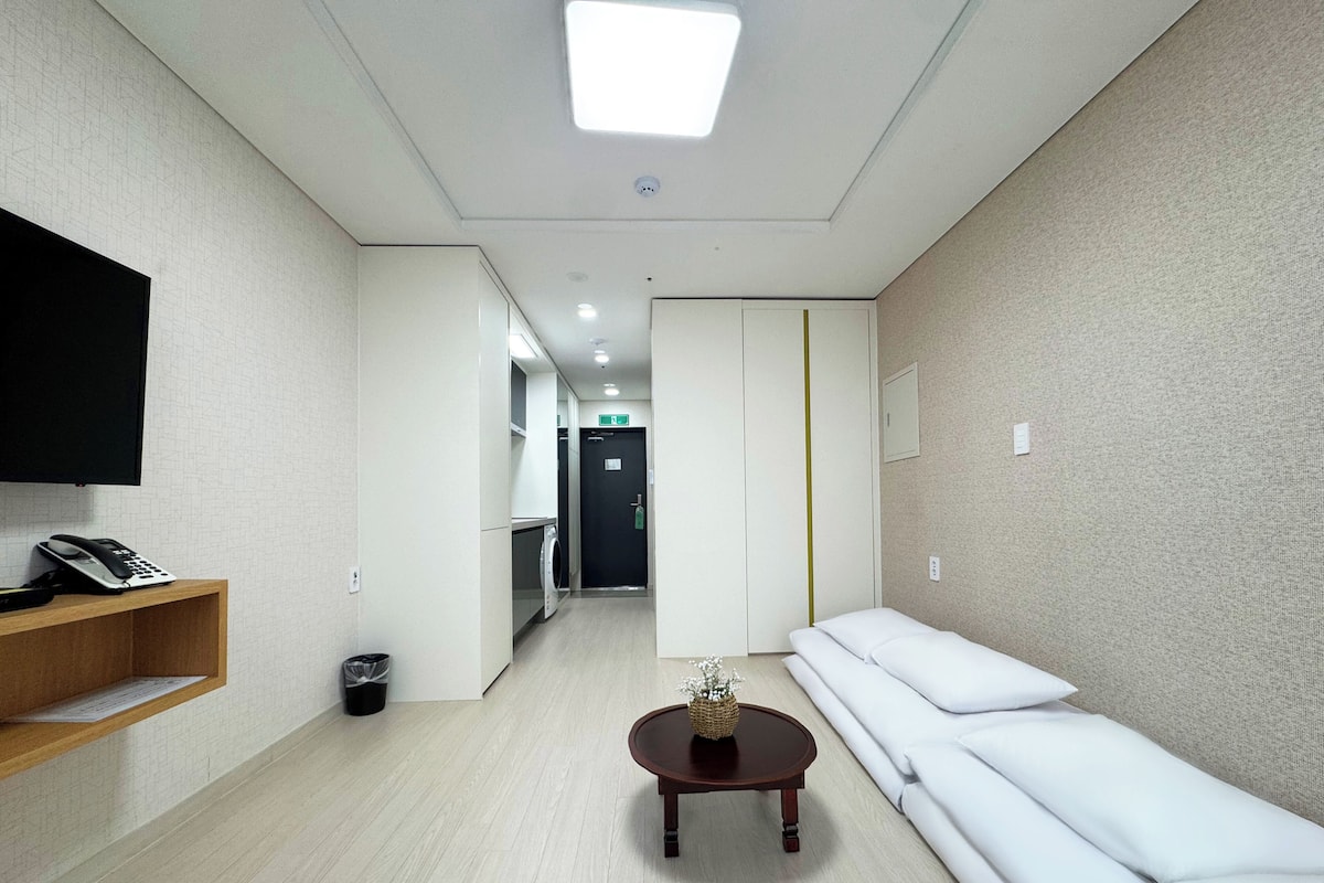 A hotel lobby with a reception desk, a sofa, a small table, and a TV mounted on the wall.