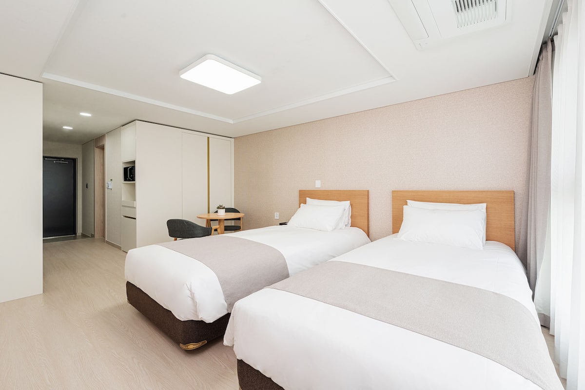 A hotel room with two beds, a desk, a chair, and a mirror.