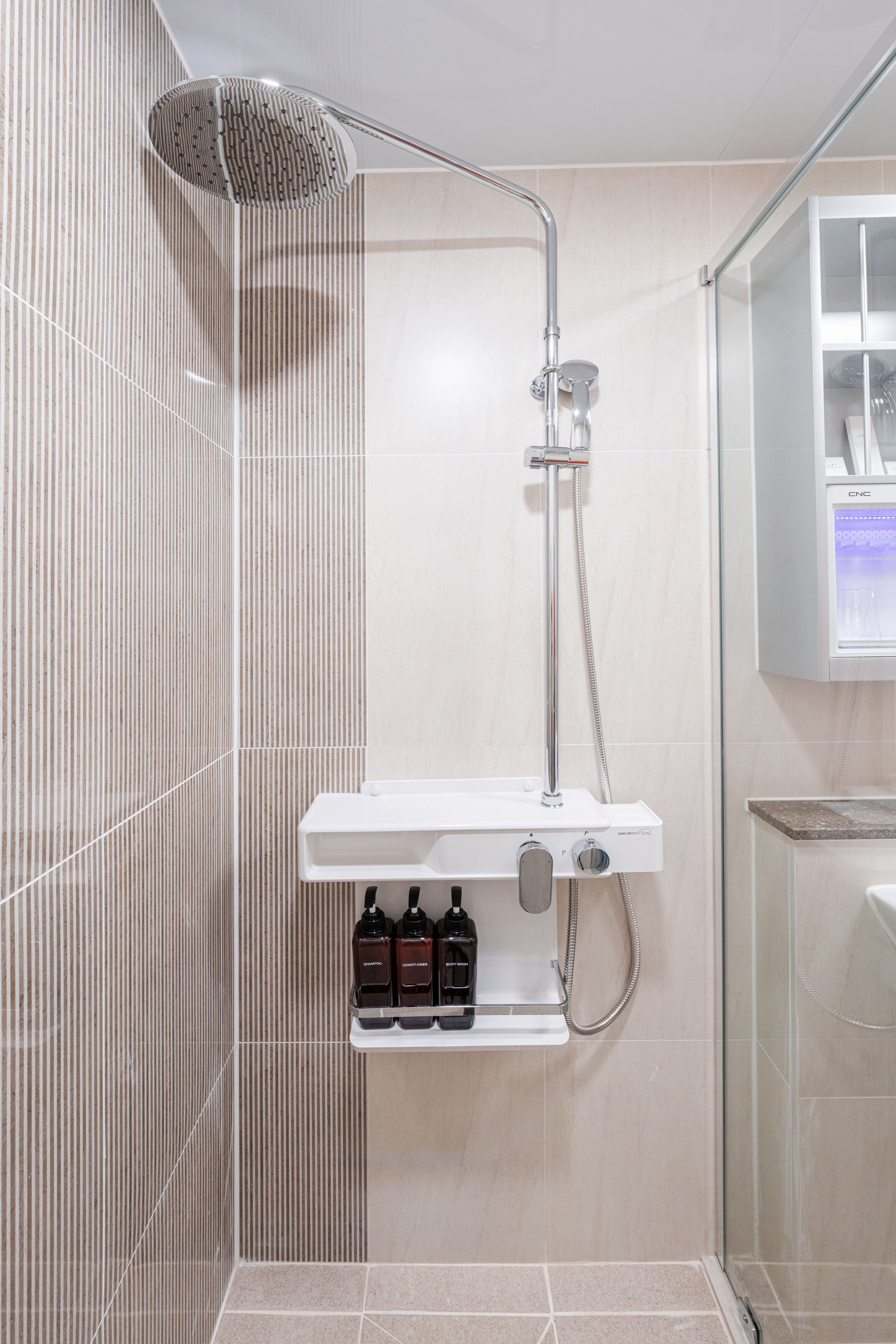 A modern shower with a handheld showerhead, a wall-mounted faucet, and a shelf with toiletries.