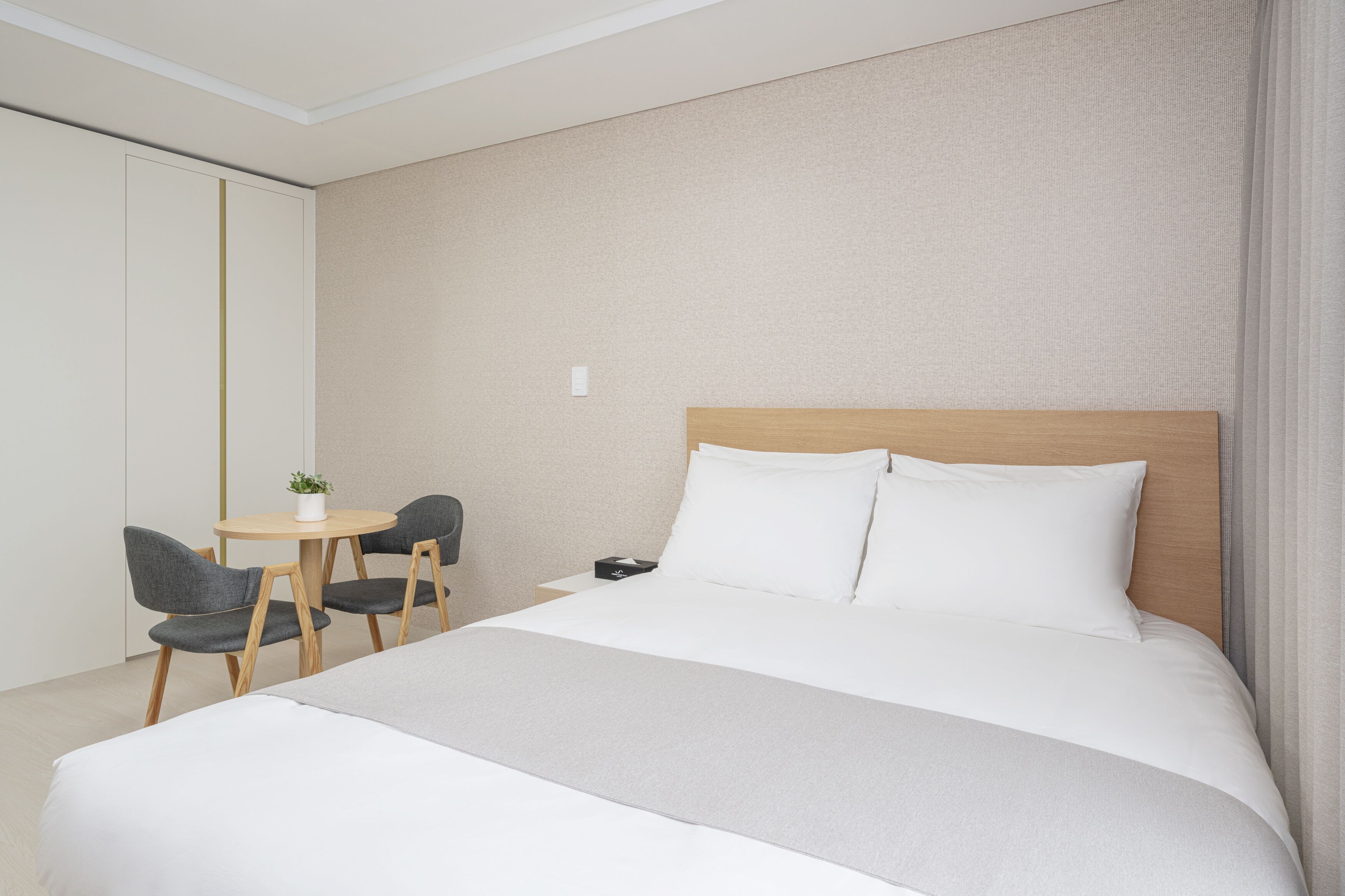 A hotel room with a large bed, a small round table with two chairs, a nightstand, and a wall-mounted TV.