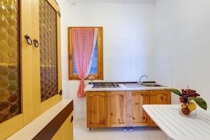 Eine Küche mit Holzschränken, einer weißen Arbeitsplatte, einem Spülbecken und einem Fenster mit kariertem Vorhang.