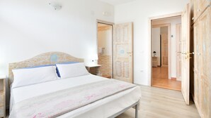 Ett sovrum med en säng, sängbord, en trädörr och en hall som leder till ett annat rum.