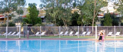 A swimming pool with white lounge chairs and a white fence.