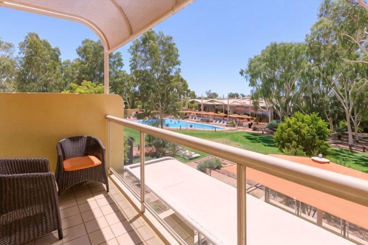 A balcony with wicker furniture, a pool, and a view of the surrounding landscape.