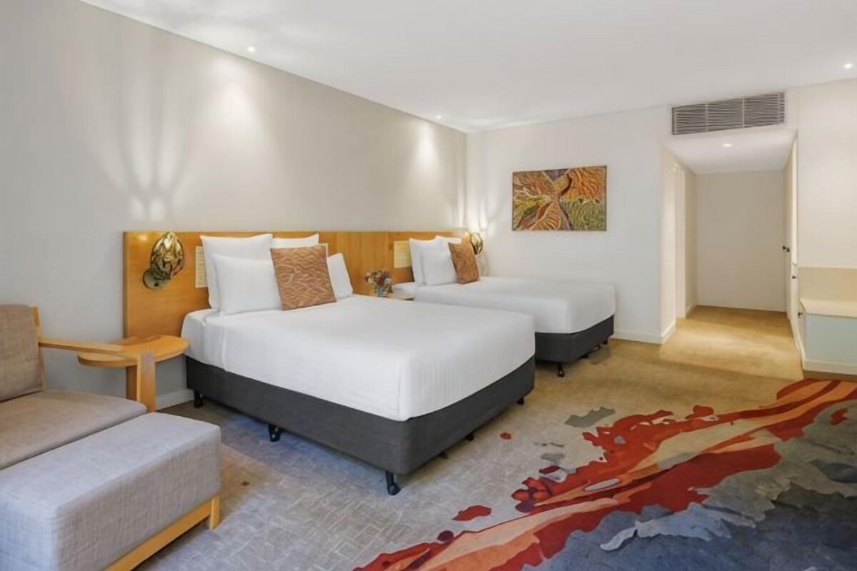 A hotel room with two beds, a sofa, a carpet, and a painting on the wall.
