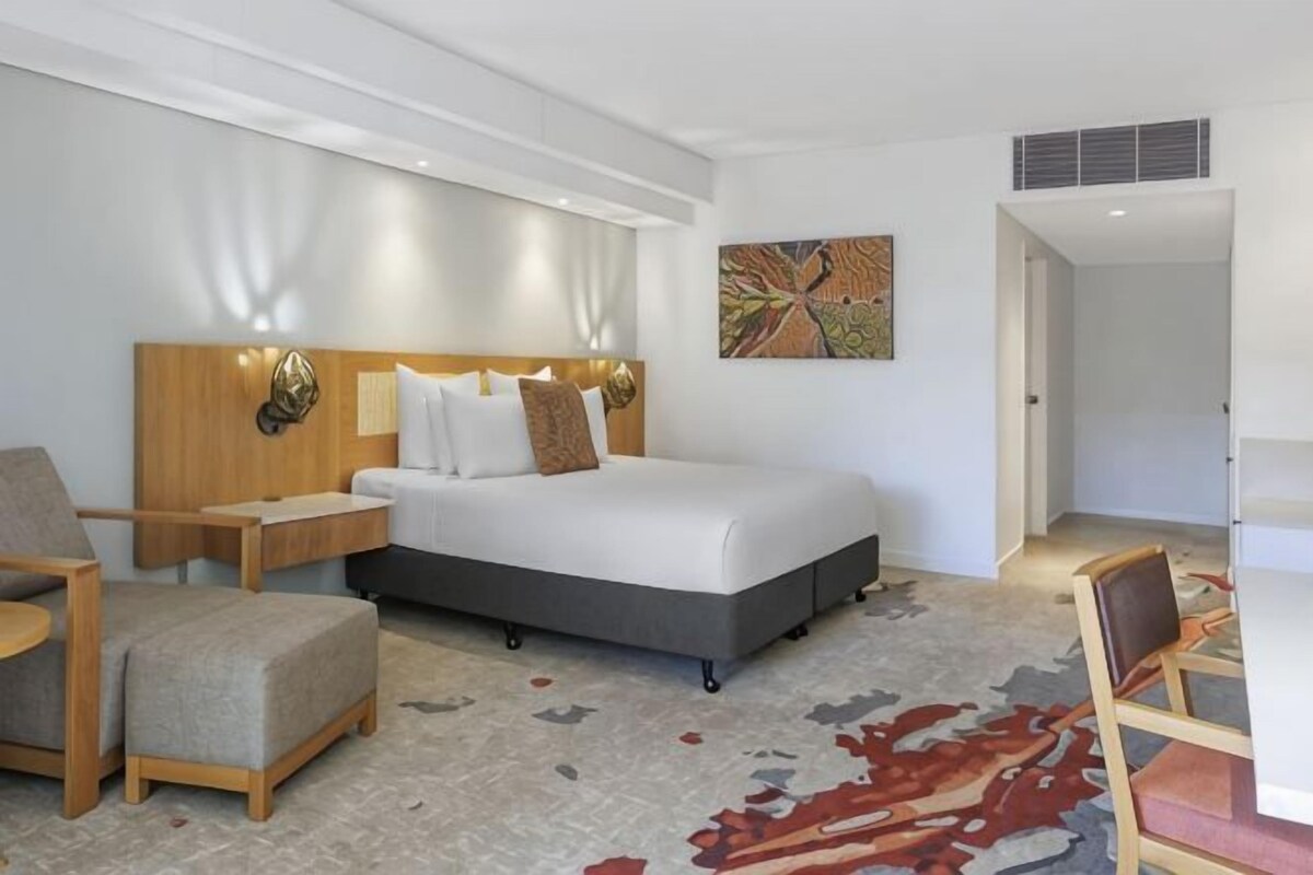 A hotel room with a bed, nightstands, a chair, a rug, and a painting on the wall.